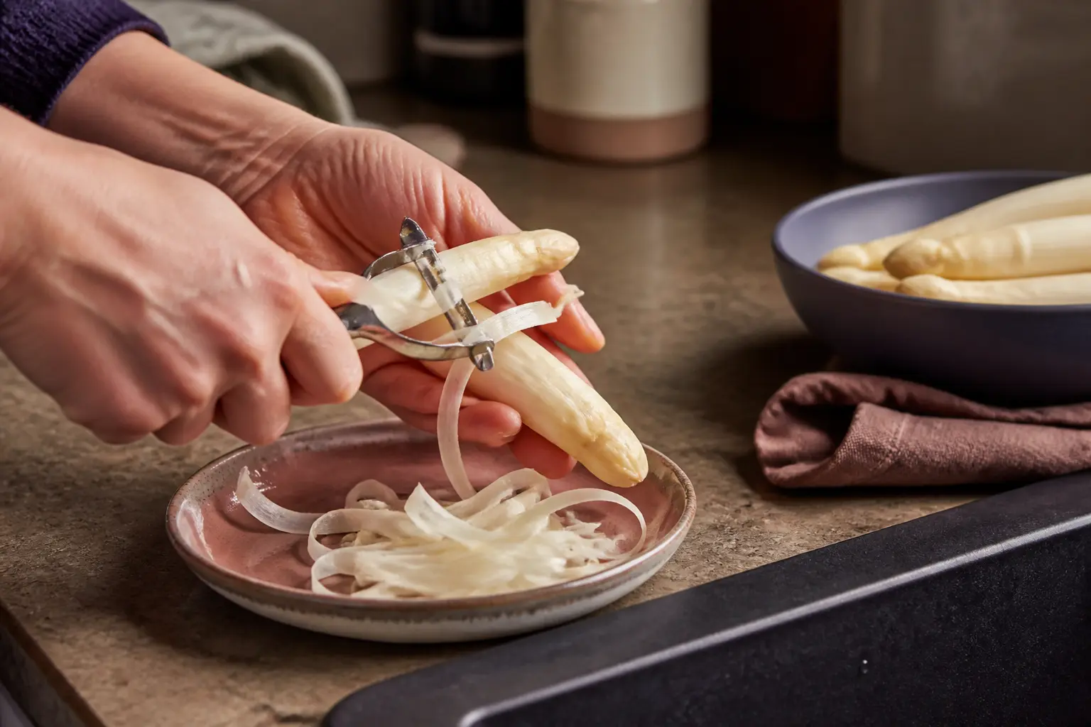 Mains épluchant des asperges blanches sur un plan de cuisine, pour la cuisson asperges blanches, lumière naturelle douce
