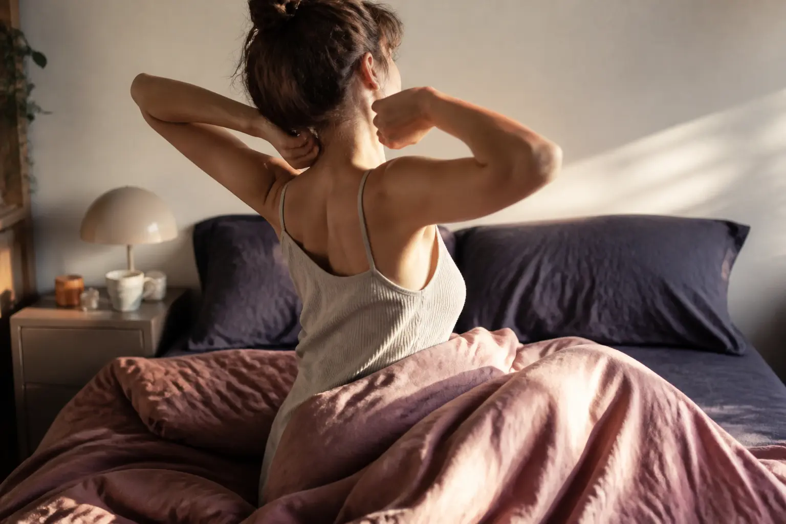 Personne se réveillant dans un lit défait, chambre douce au matin, illustrant une cure de sommeil apaisante