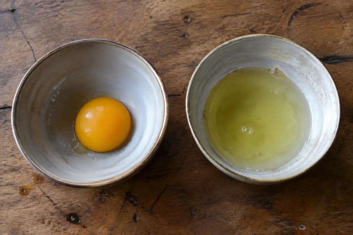 Un jaune d'œuf et un blanc séparés dans deux bols sur une table en bois