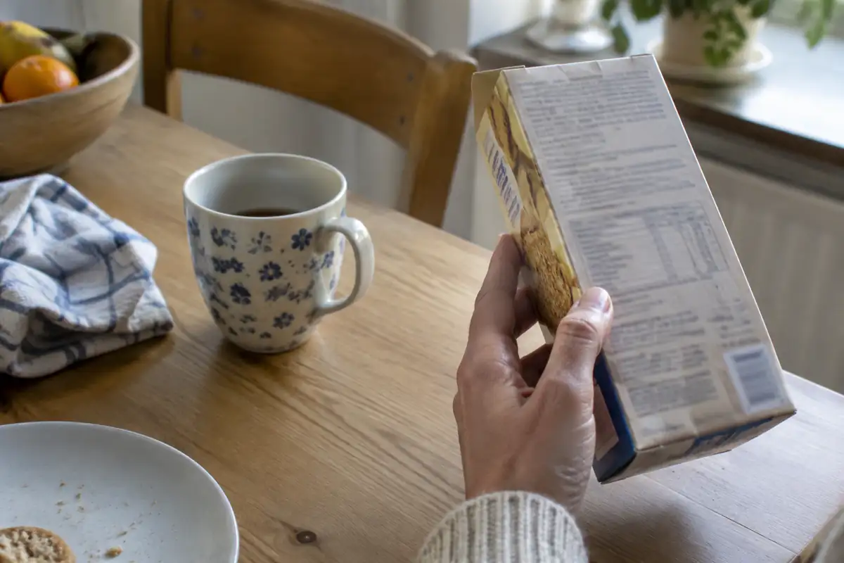 Main qui retourne un paquet de biscuits pour en lire le dos, une tasse et une assiette sur la table