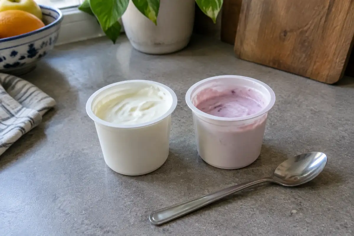 Deux pots de fromage blanc côte à côte, l'un nature et l'autre aux fruits, avec une cuillère