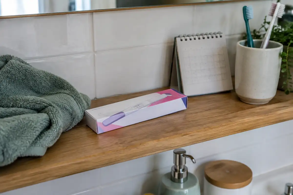 Boîte de test de grossesse fermée sur une étagère de salle de bains, à côté d'un petit calendrier